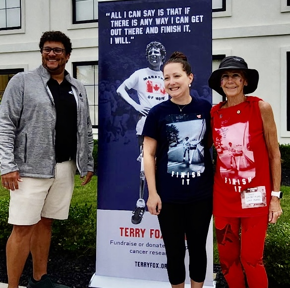Marilyn Farnworth in red with two fellow participants beside a Terry Fox banner.
