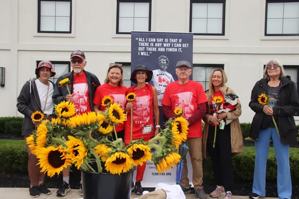 Marilyn Farnworth and fellow Terry Fox Run participants gathered with sunflowers beside a Terry Fox banner.