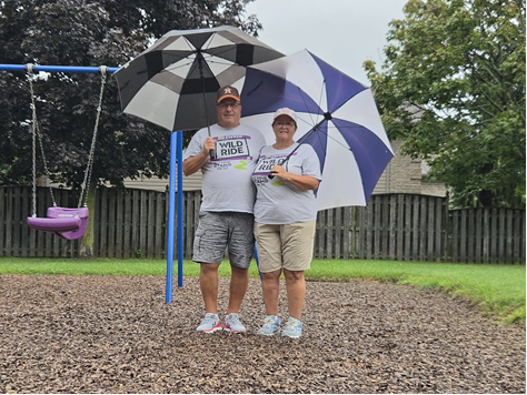 Two Wild Ride participants holding umbrellas beside a swing set.